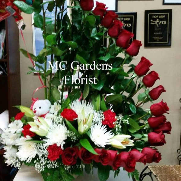 Tall arrangement of red roses and white lilies with a teddy bear