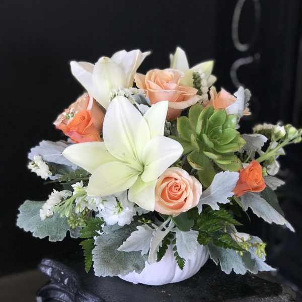 Peach roses and white lilies in a white pumpkin container