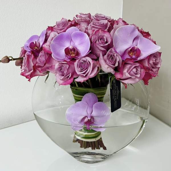 Pink roses and lavender orchids arranged in a clear glass vase