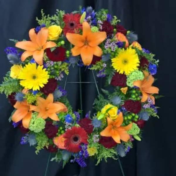 Colorful floral wreath on a stand with orange lilies and yellow daisies