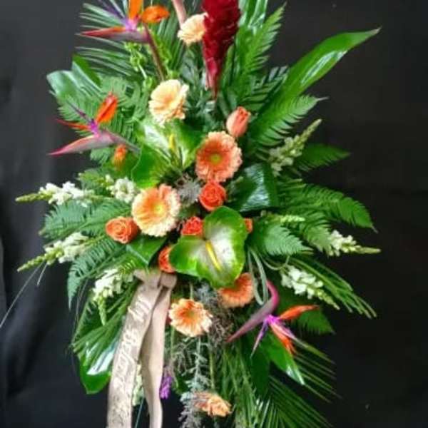 Tall tropical standing spray with orange and peach flowers on a black easel