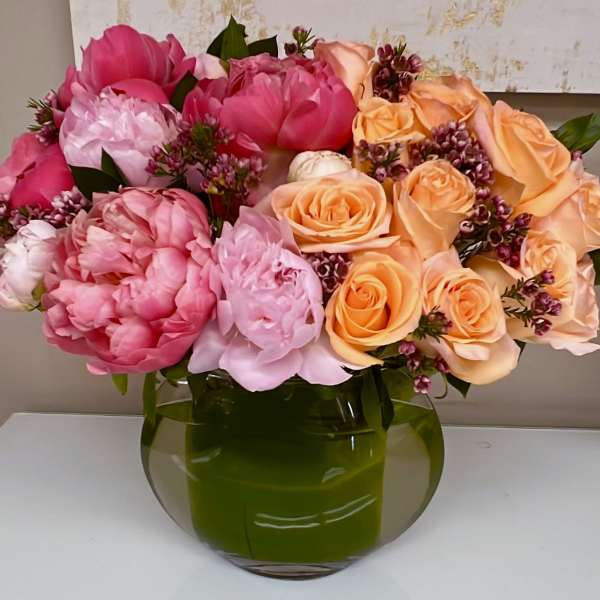 Pink and peach roses with peonies in a green glass vase