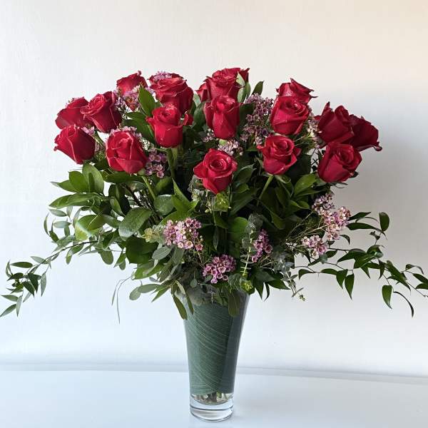 Red roses arranged in a tall glass vase with small pink filler flowers