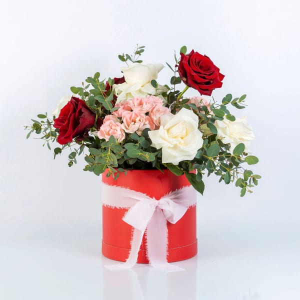 Red and white roses with pink carnations in a red box tied with a white ribbon