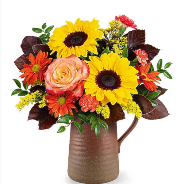 Bouquet of sunflowers, roses, and orange daisies in a brown pitcher vase
