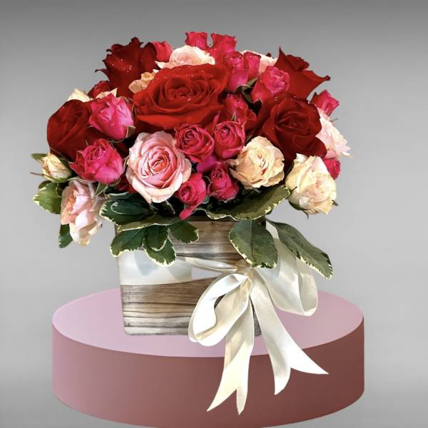 Bouquet of red, pink, and cream roses in a wooden box with a ribbon