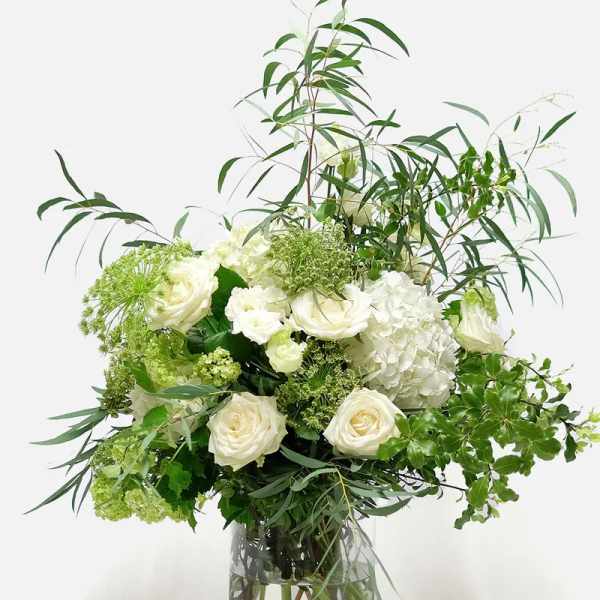 White roses and hydrangeas in a clear glass vase with airy greenery