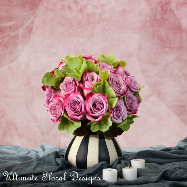 Pink and lavender roses in a striped vase with small candles nearby