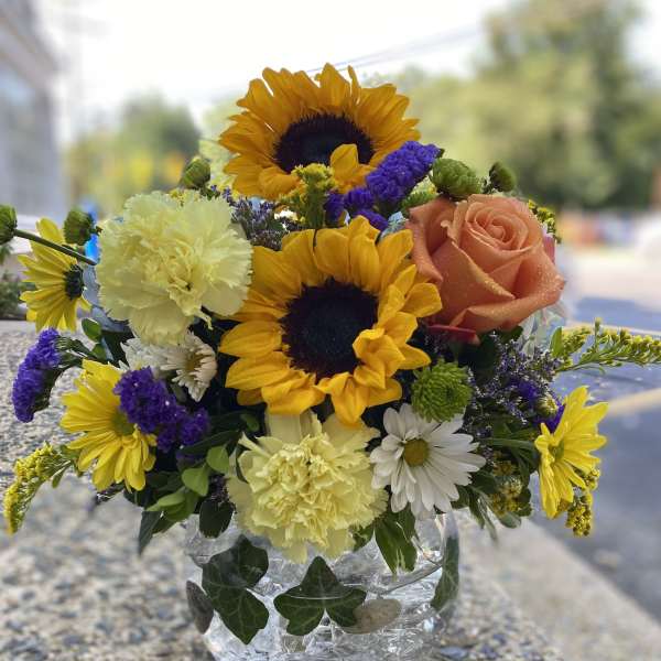 Mixed bouquet in a clear glass vase with sunflowers, a peach rose, and carnations