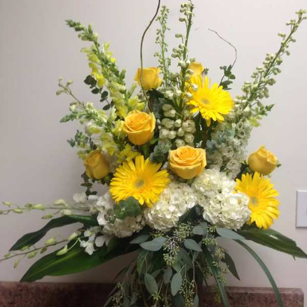 Yellow roses and gerbera daisies in a vase with white hydrangeas