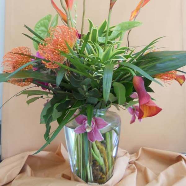 Tropical flower arrangement in a clear glass vase with orange bird-of-paradise and pink calla lilies