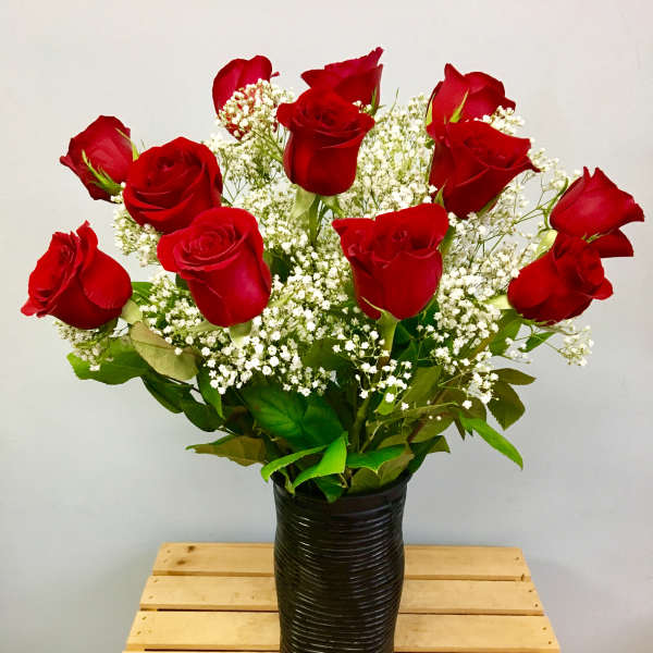 Red roses arranged in a black vase with white filler flowers