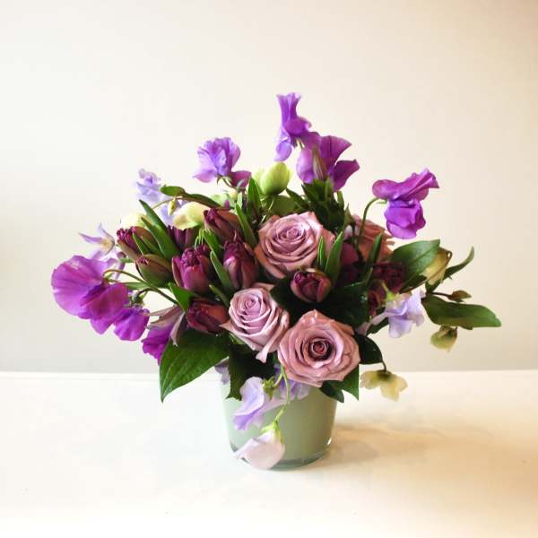 Purple and blush roses arranged in a glass vase