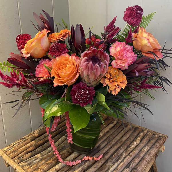 Bright mixed bouquet with orange roses and a protea in a green vase