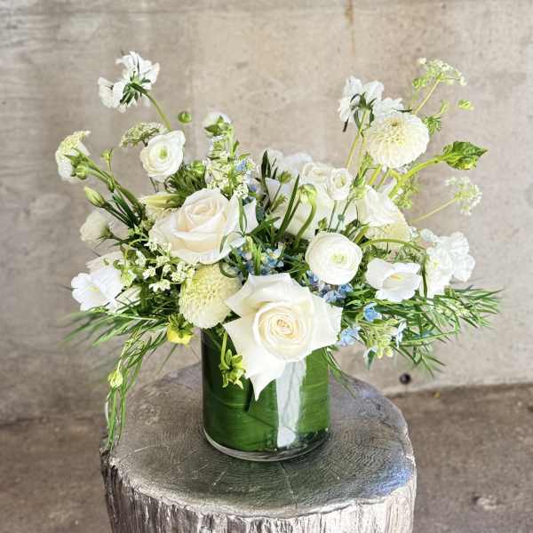 White floral arrangement in a glass vase with roses and round blooms