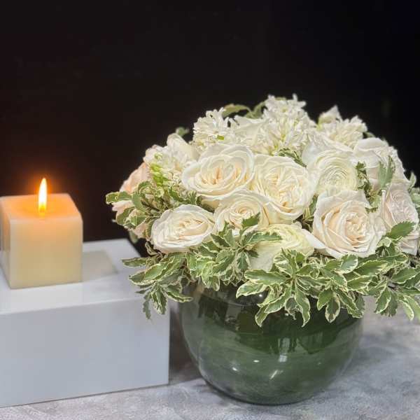 White rose bouquet in a glass vase beside a lit candle