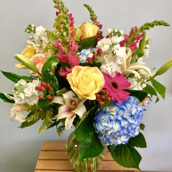 Mixed bouquet of roses, hydrangea, lilies, and gerbera daisies in a glass vase