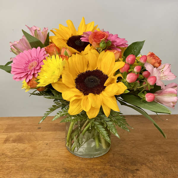 Mixed bouquet with sunflowers, pink gerberas, and roses in a glass vase