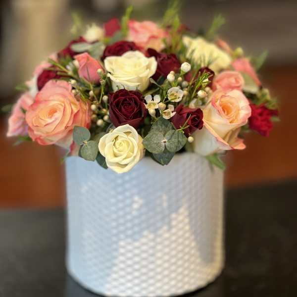 Bouquet of pink, cream, and burgundy roses in a white textured vase