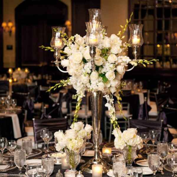White floral centerpiece with candles in tall glass holders on a banquet table