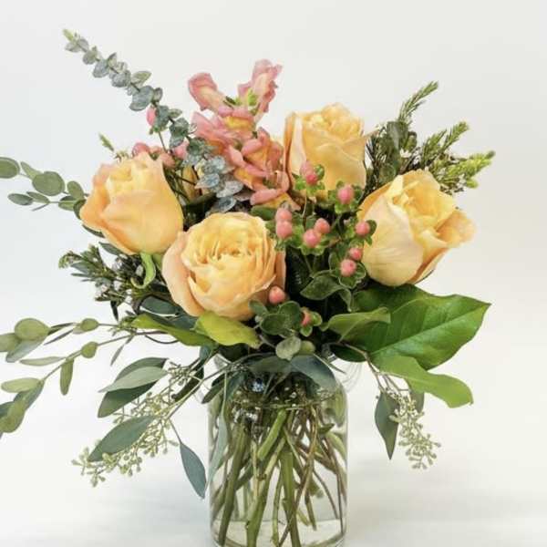 Peach roses arranged in a clear glass vase with mixed greenery