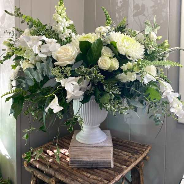 White floral arrangement in a white urn vase