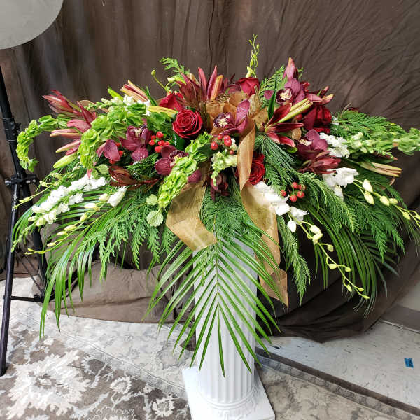 Large floral spray with red roses, burgundy orchids, and white blooms on a pedestal