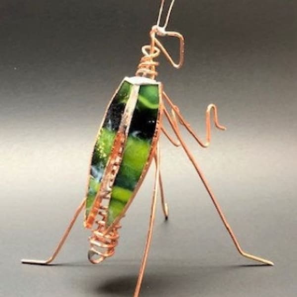 Copper wire insect sculpture with green stained glass body on a dark background