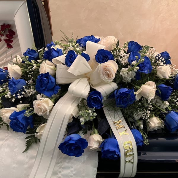 Blue and white rose arrangement with a ribbon on a casket