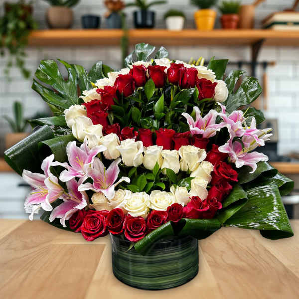 Red and white rose arrangement with pink lilies in a green vase