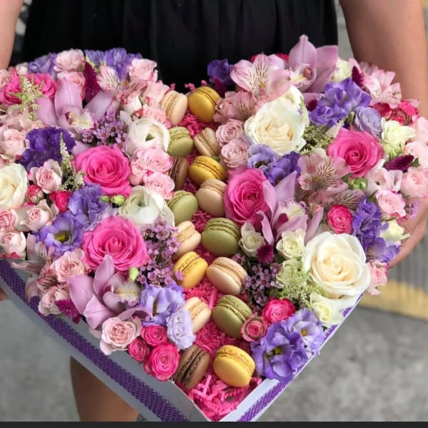 Heart-shaped box of pink and purple flowers with macarons