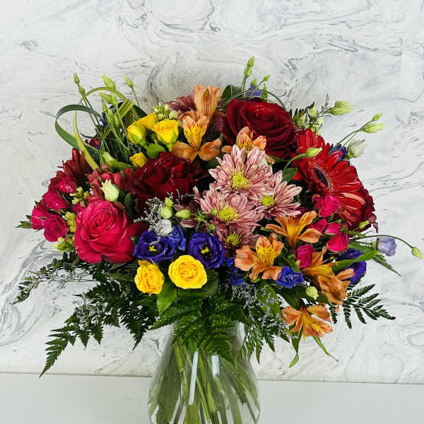 Colorful mixed bouquet in a clear glass vase with roses and daisies