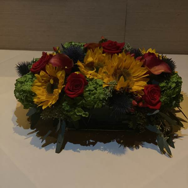 Low floral centerpiece with sunflowers, red roses, and calla lilies