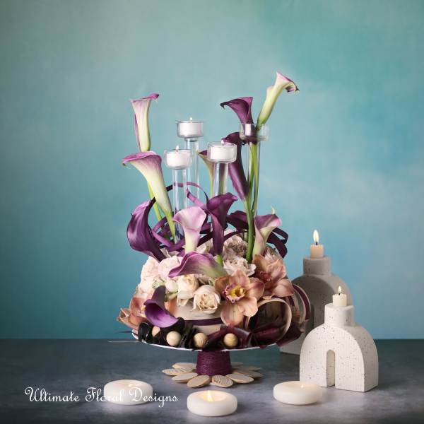 Purple calla lilies and roses arranged with candles on a pedestal