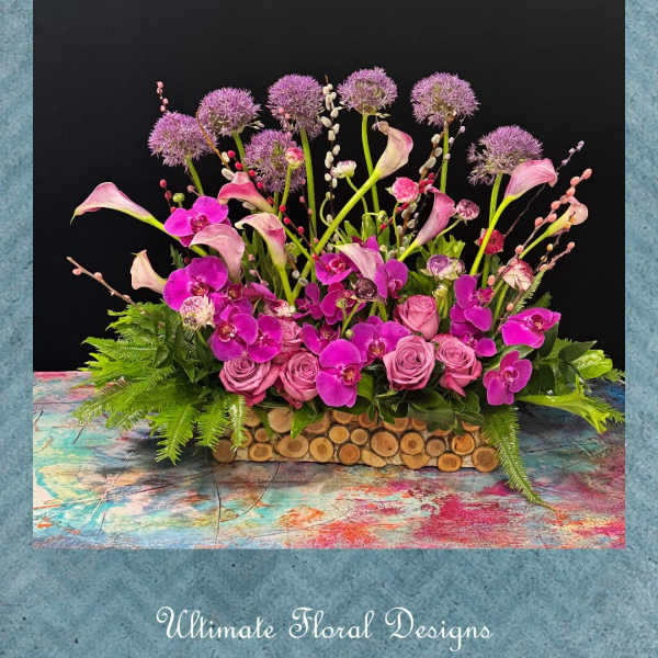 Pink and purple floral arrangement with calla lilies, orchids, and roses in a wooden container