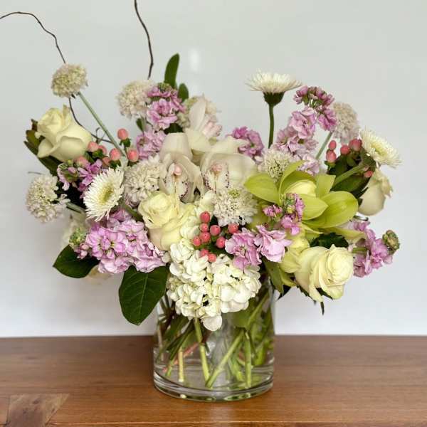 Mixed bouquet of cream, pink, and green flowers in a clear glass vase