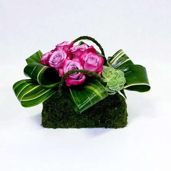 Pink roses in a moss-covered basket with striped leaves and a green succulent