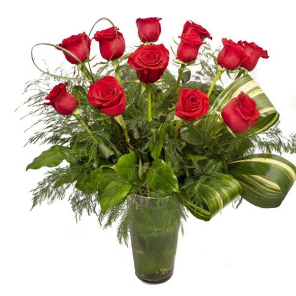 Red roses arranged in a clear glass vase with greenery
