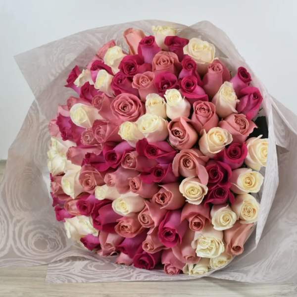Large hand-tied bouquet of cream, blush, and hot pink roses wrapped in sheer patterned paper.
