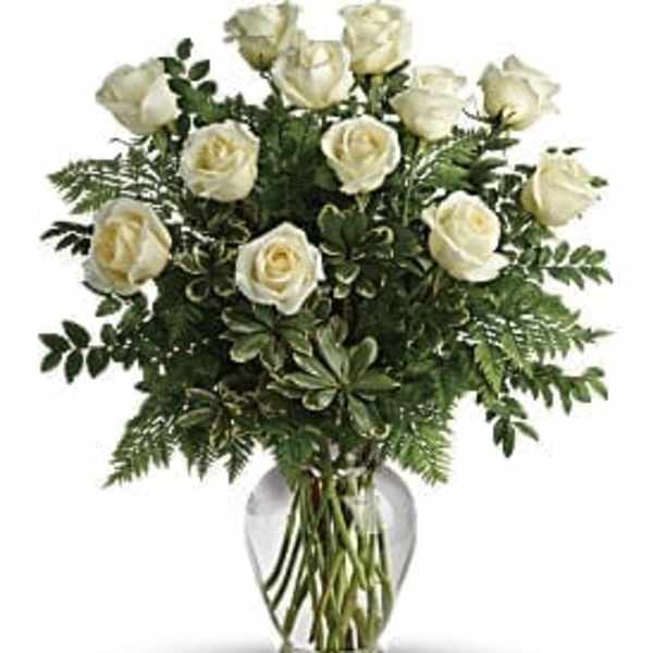 White roses arranged in a clear glass vase with greenery