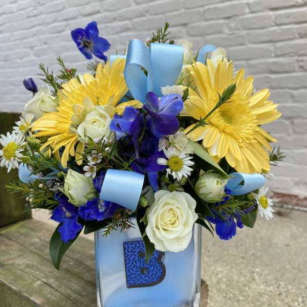 Yellow daisies and white roses in a glass vase with blue ribbon