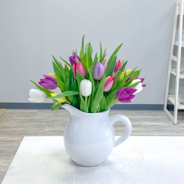 Mixed tulip arrangement in a white ceramic pitcher on a light table