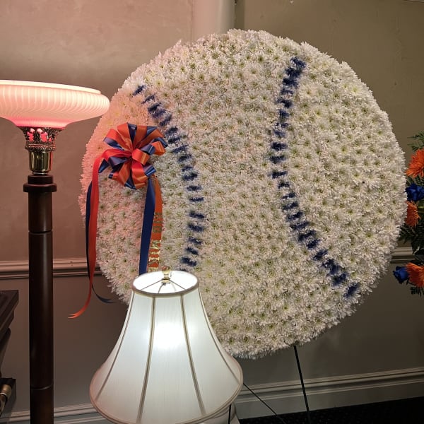 Large white floral wreath with blue lettering and a red-blue ribbon bow