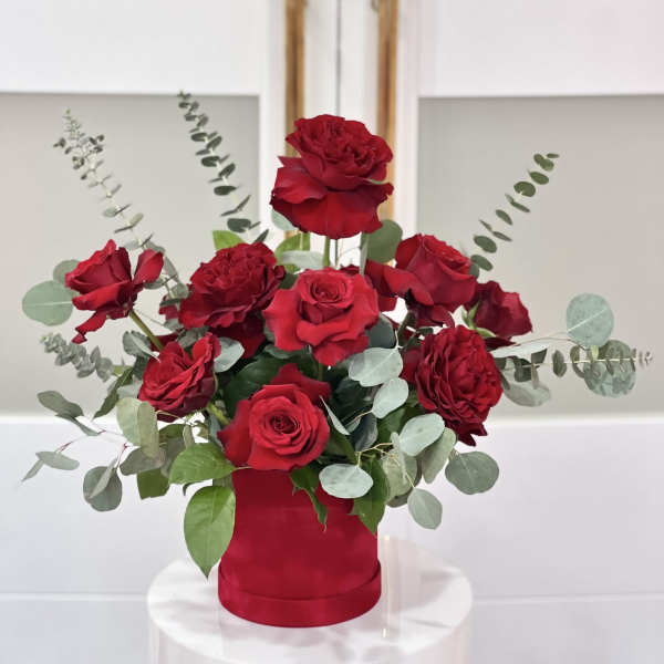 Red roses arranged in a red cylindrical vase with eucalyptus accents