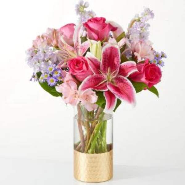 Pink roses and lilies in a clear glass vase with a gold wrap