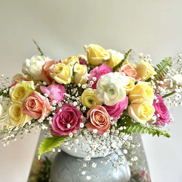 Mixed roses in pink, yellow, peach, and white arranged in a white vase