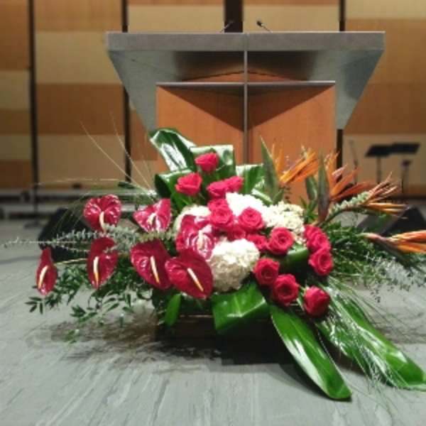 Large red and white podium floral arrangement with roses, hydrangeas, and tropical blooms on a stage