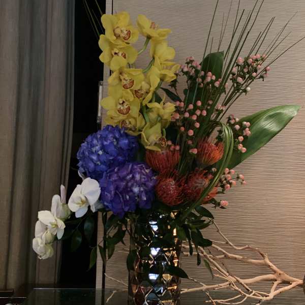 Tall mixed floral arrangement in a metallic vase with orchids and hydrangeas