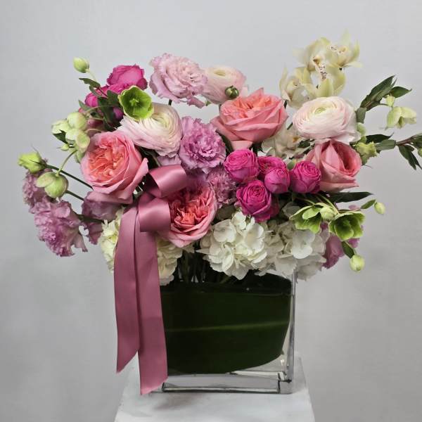 Pink and white floral arrangement in a clear square vase with a satin ribbon
