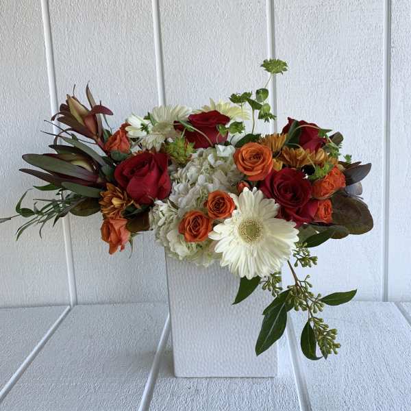 Mixed bouquet of red and orange roses with white daisies in a white vase